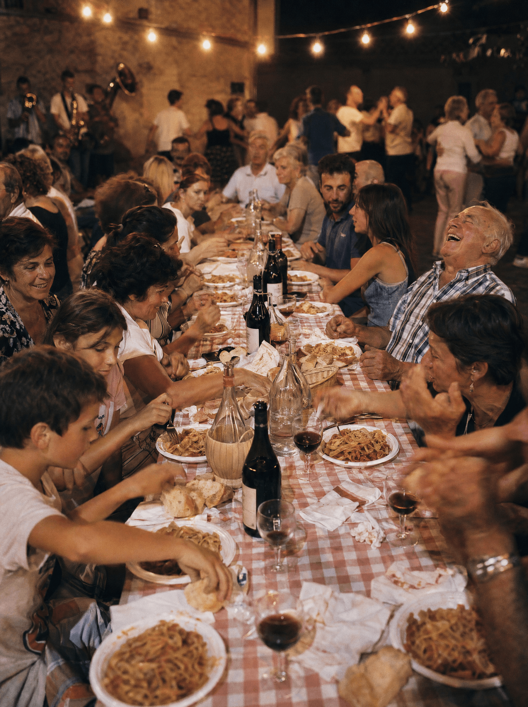 Tavolata di paese sotto le lampadine, vino rosso e pasta lunga